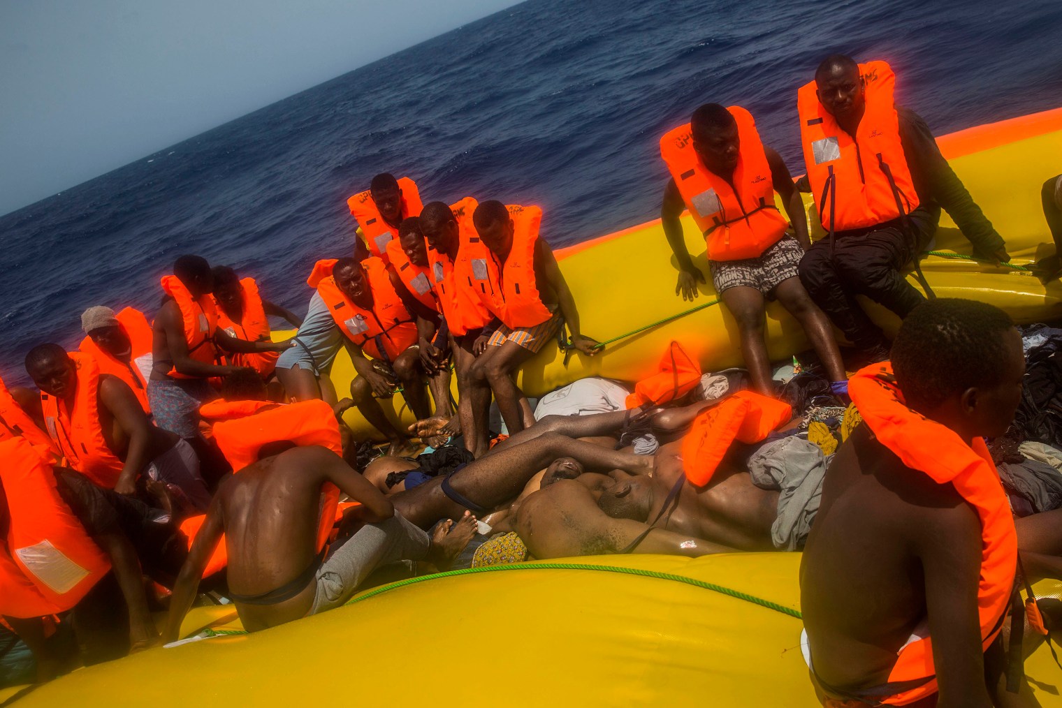 Migrants waiting to be rescued sit on the edge of the rubber boat, around a pile of bodies.