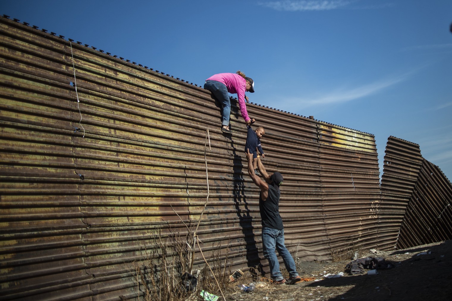 A group of Central American migrants near the El Chaparral crossing in Tijuana climb the fence between Mexico and the U.S. on Nov. 25, a day of turmoil at the border.